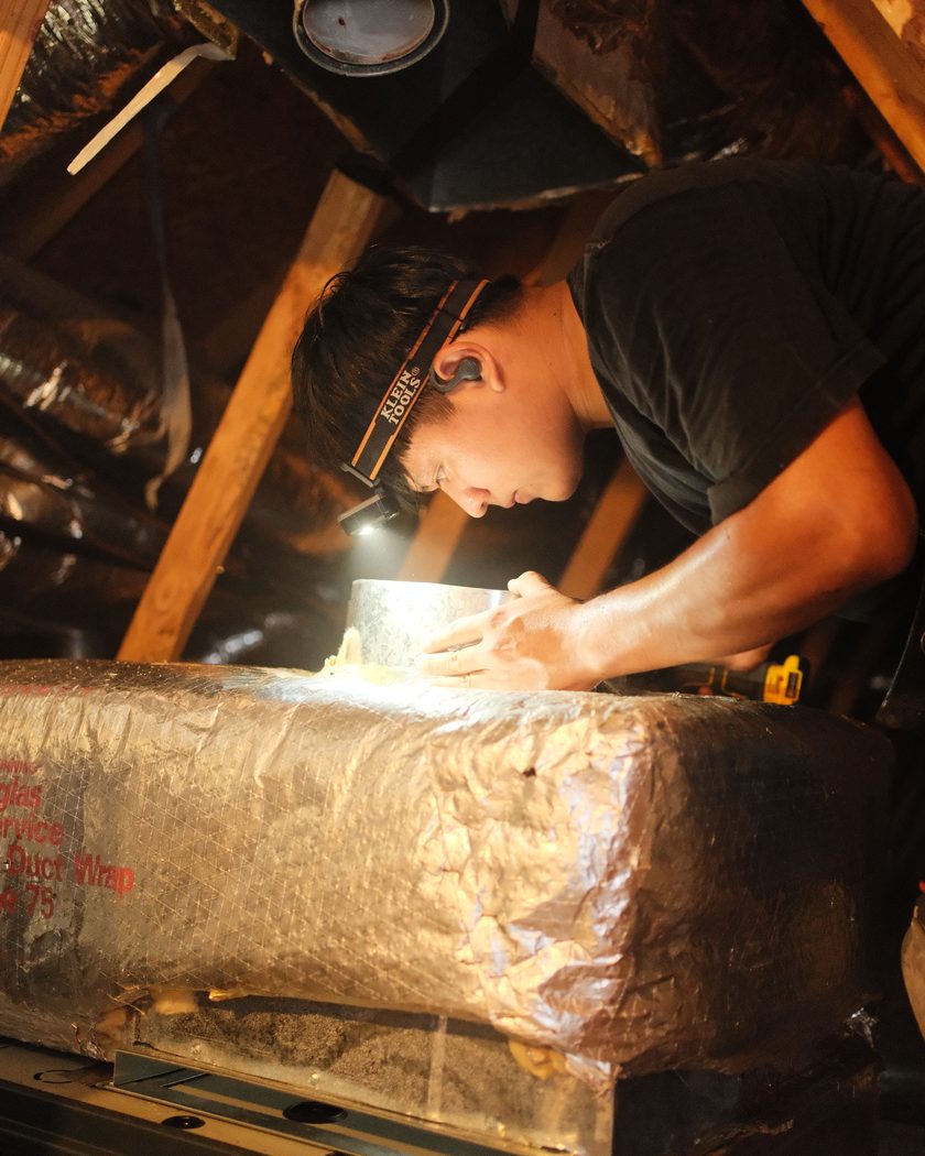 A technician sealing duct work by headlamp in an Atlanta attic.