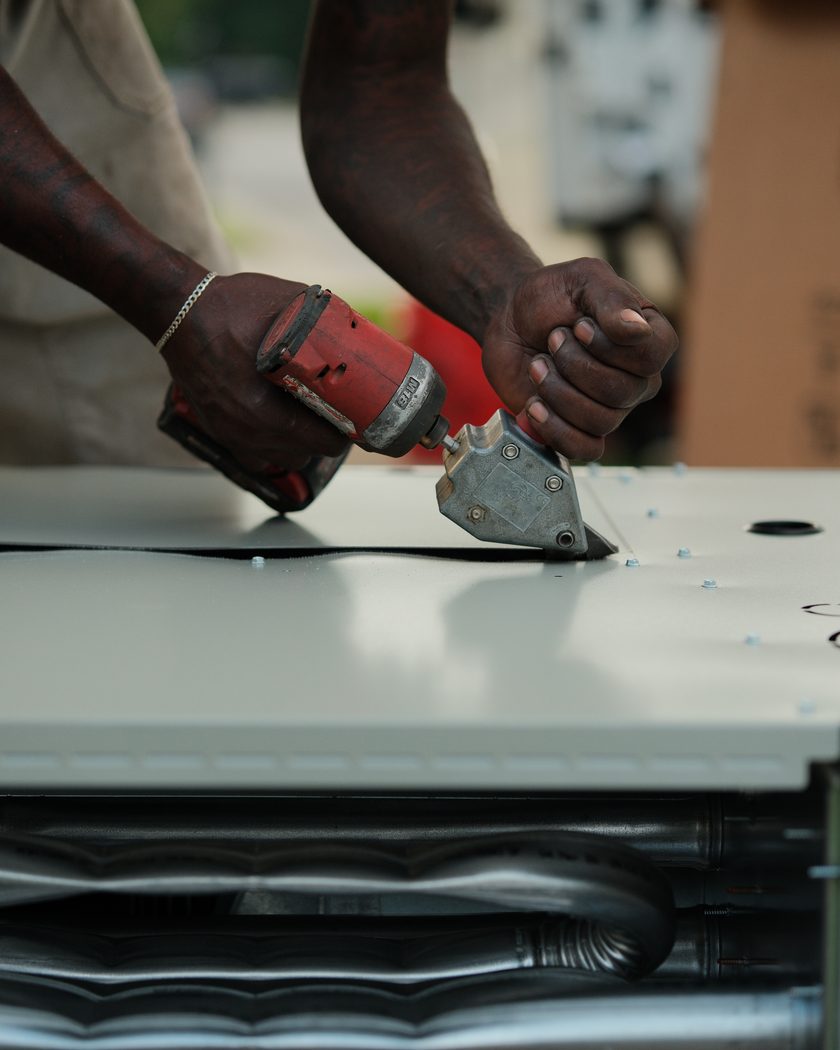 Close-up of a technician's hands fastening a panel on a new condenser coil.