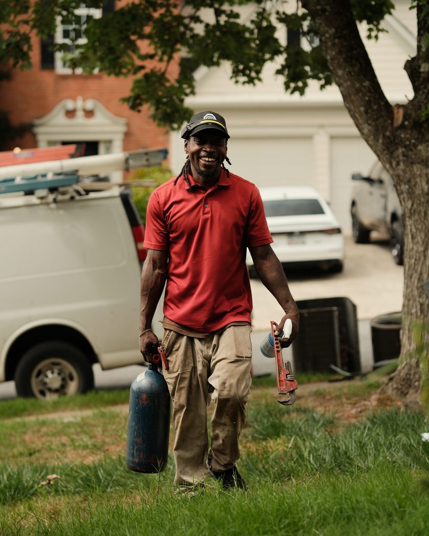 An Atlanta Metro Airflow technician walking up to a home, tools in hand, with the company van parked at the curb.