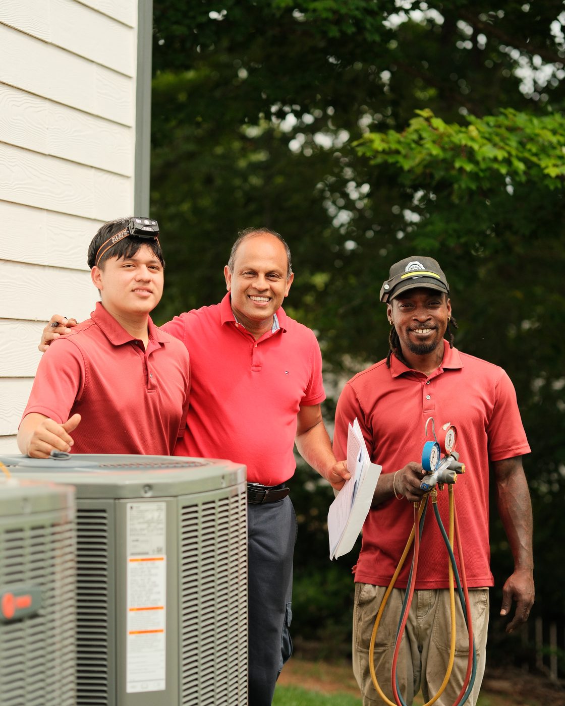 The Atlanta Metro Airflow crew of three, smiling together beside an outdoor condenser unit at an Atlanta home.